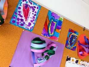 A variety of heart-themed, colorful children's artwork on a bulletin board.