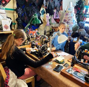 Two girls sew on old-fashioned sewing machines in a quilting studio.